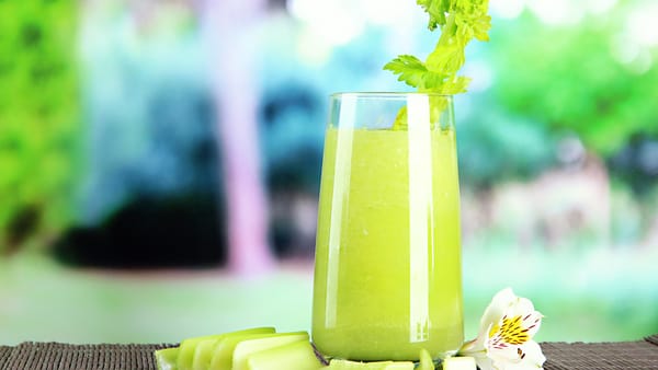 A glass of fresh celery juice with celery stalks